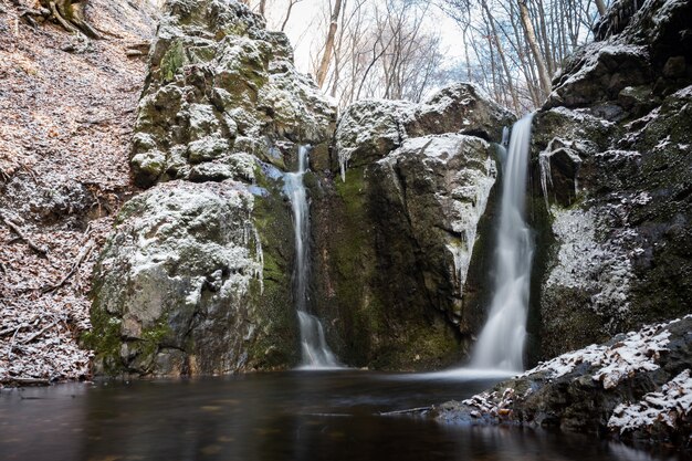 Horizontal shot of several waterfalls coming out of huge snowy rocks in the winter season