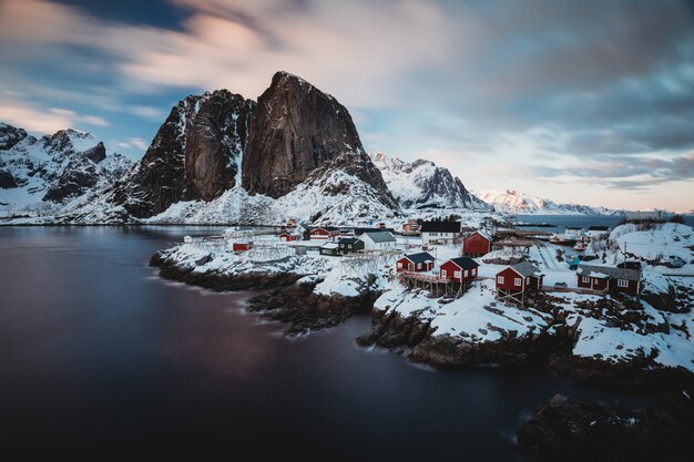 Horizontal shot of a shore town with red houses near a sea and a snowy mountain in the back