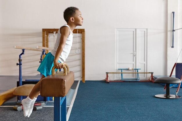 Horizontal shot of skillful atheltic Afro American boy in sportswear mounting on pommel horse