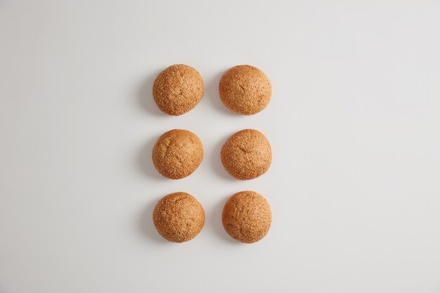 Horizontal shot of soft small round sesame burger buns for preparing delicious hambrugers or sandwiches. Nourishing crusty brioches isolated on white surface. Fast food, unhealthy eating.