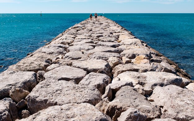 Horizontal shot of a stone pathway on a body of water with people walking on it.