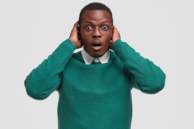 Horizontal shot of stupefied dark skinned man keeps hand on head, stares in stupor, has short Afro haircut