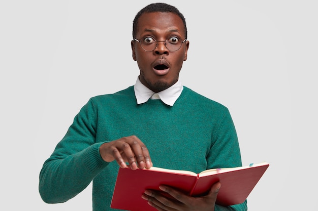 Horizontal shot of surprised scared black man stares  with popped eyes, reads book