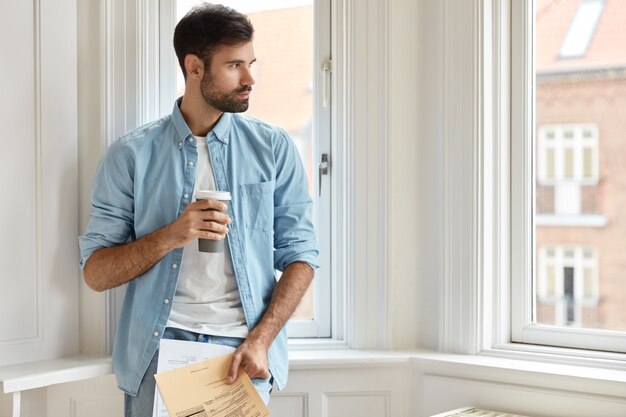 Horizontal shot of thoughtful bearded male working at home