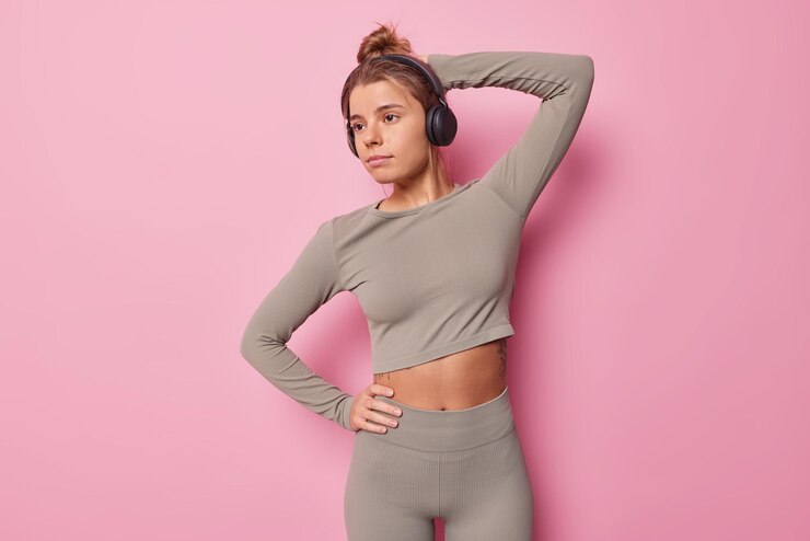 Free Photo horizontal shot of thoughtful sporty woman dressed in cropped top and leggings has good fit body listens music during training isolated over pink background. people sport and healthy lifestyle