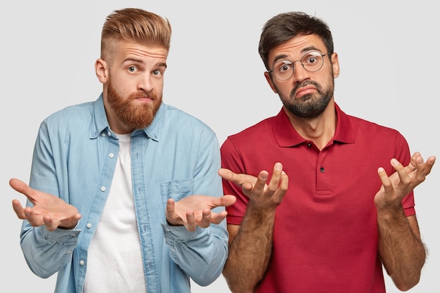 Horizontal shot of two bearded guys have clueless hesitant expressions, spread palms in bewilderment