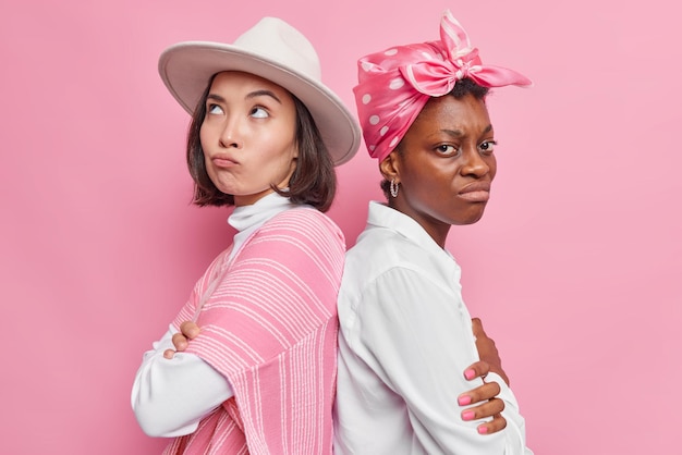 Horizontal shot of upset offended women feel angry after quarrel stand backs to each other keeps arms folded do not speak isolated over pink background sort out relationships. Negative emotions