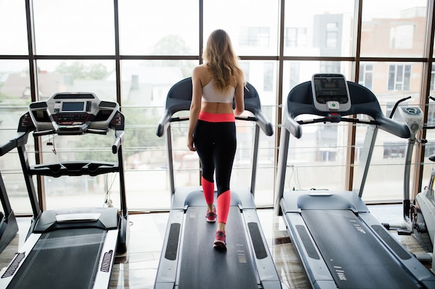 Foto gratuita inquadratura orizzontale della donna che pareggia sul tapis roulant al centro benessere. donna che lavora in una palestra in esecuzione su un tapis roulant.