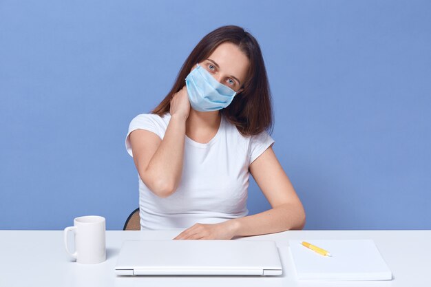 Horizontal shot of woman working at laptop at home, lady having distance work, posing at desk isolated over blue