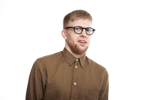Free photo horizontal shot of young bearded male of european appearance wearing eyeglasses and shirt having disgusted displeased expression, staring with disgust. human emotions and reaction