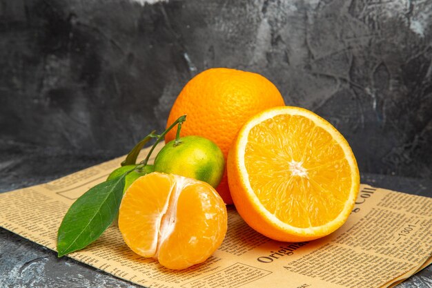 Horizontal view of citrus fruits in cut and whole form with leaves on newspaper on gray background