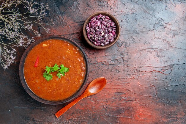 Горизонтальный вид классического томатного супа в коричневой миске с фасолью и ложкой на столе смешанного цвета