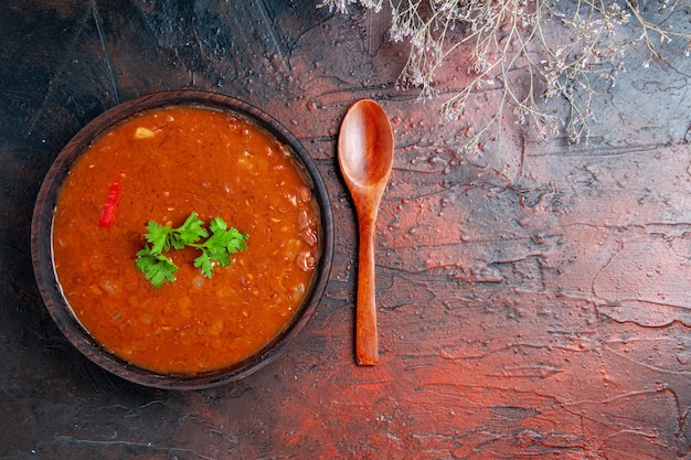 Horizontal view of classic tomato soup in a brown bowl and spoon on mixed color table