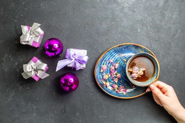 Горизонтальный вид красочных подарков и украшений с чашкой черного чая на темном фоне