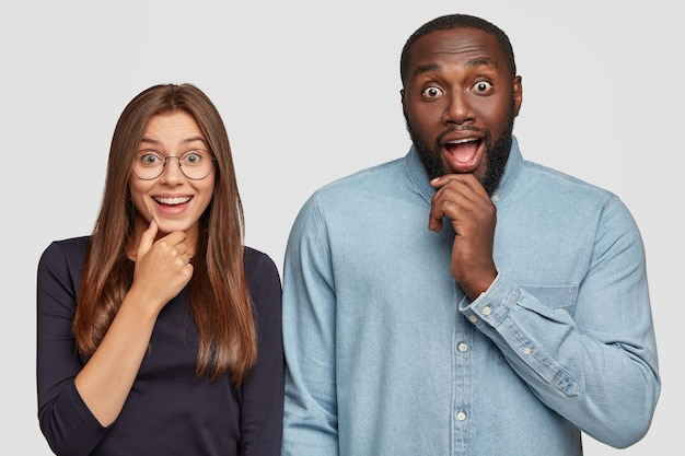 Horizontal view of curious emotional surprised diverse girlfriend and boyfriend keeps jaw dropped from amazement