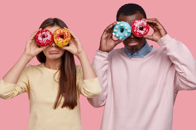 Horizontal view of dejected mixed race lady and guy cover eyes with delicious, dressed jumpers, going to have sweet snack