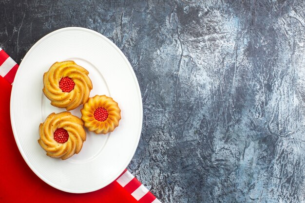 Horizontal view of delicious biscuits on a white plate on red towel on dark surface