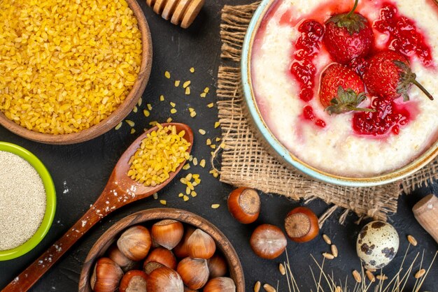 Horizontal view of delicious breakfast served with strawberries jam in a bowl and spikes hazelnuts eggs rice on dark color background