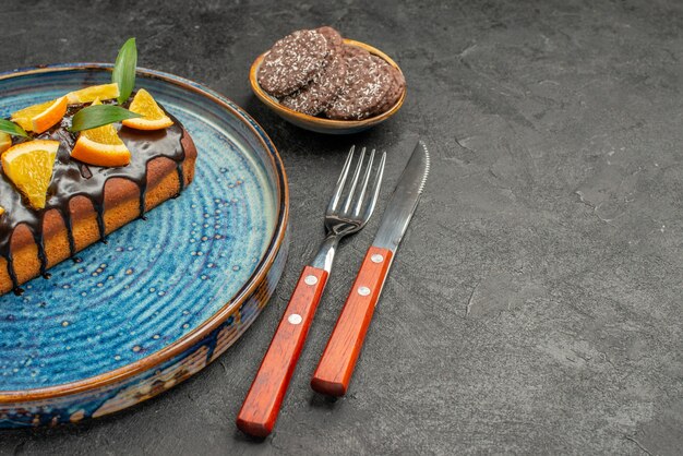 Horizontal view of delicious cake and biscuits with fork and knife on black table