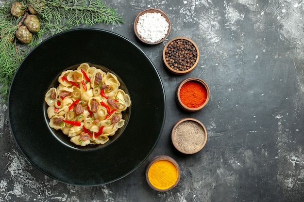 Horizontal view of delicious conchiglie with vegetables and greens on a plate and knife and different spices on gray background