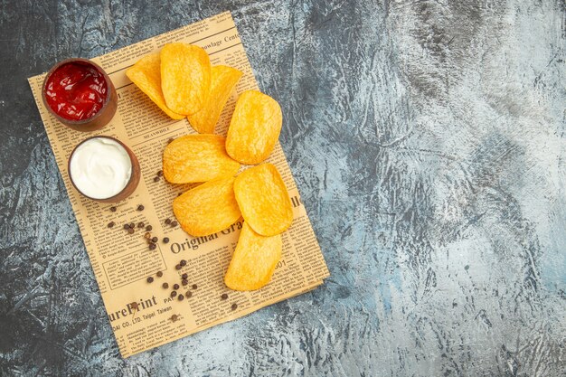 Horizontal view of delicious homemade chips and pepper bowl mayonnaise ketchup on newspaper on gray table