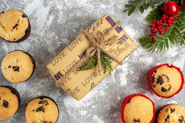 Horizontal view of delicious small cupcakes with chocolate and fir branches next to gift on ice surface