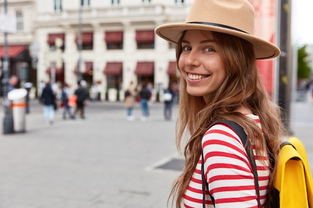 Horizontal view of delighted female tourist walks on street