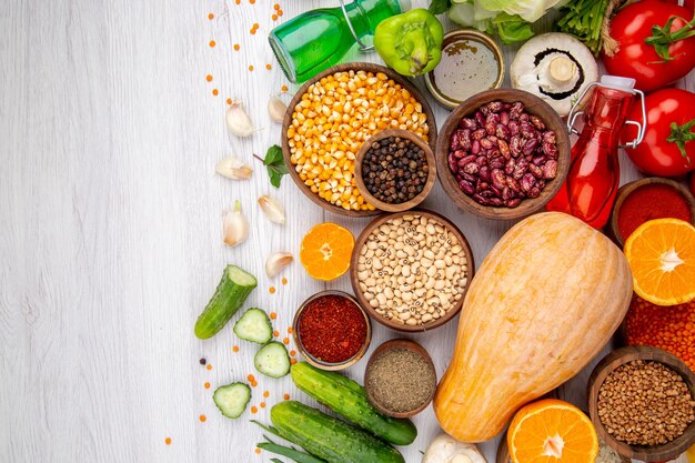 Horizontal view of fresh cauliflower and different foods for cooking on the right side on white table