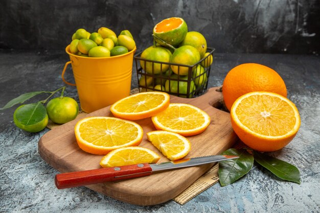 Horizontal view of fresh citrus fruits with knife on wooden cutting board on newspaper on gray background