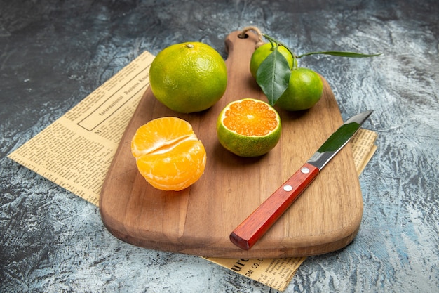 Horizontal view of fresh citrus fruits with leaves on wooden cutting board cut in half forms on newspaper on gray background