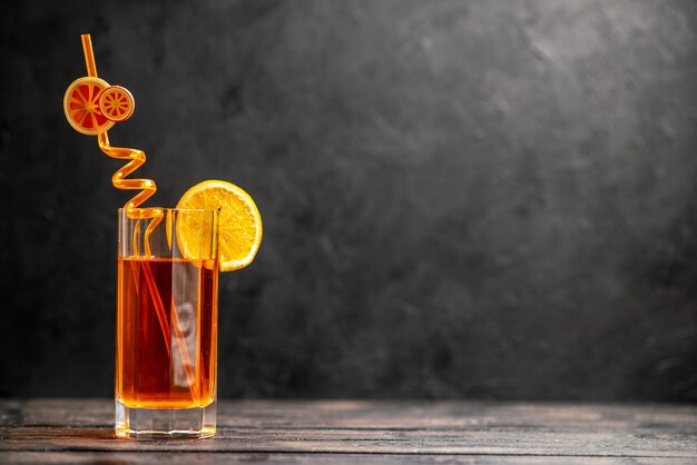 Horizontal view of fresh delicious juice in a glass with orange lime and tube on dark background