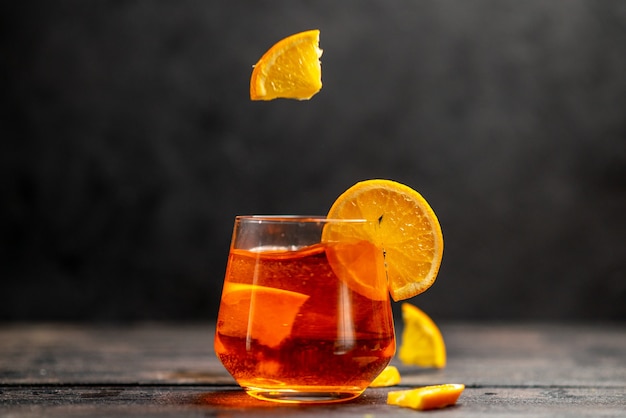 Horizontal view of fresh delicious juice in a glass with orange limes on dark background