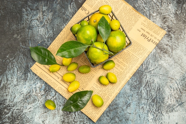 Horizontal view of fresh kumquats and lemons in a black basket on newspapers on gray background