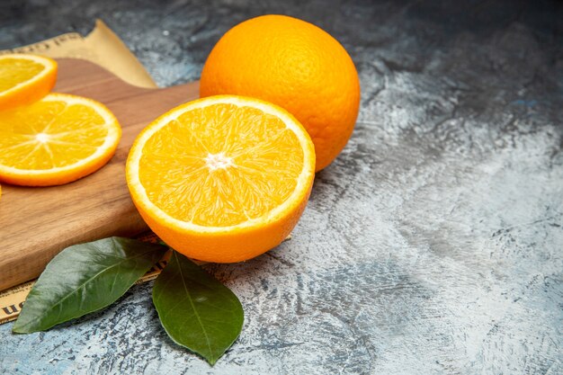 Horizontal view of fresh lemon slices on wooden cutting board on newspaper on gray background