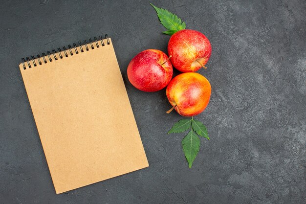 Horizontal view of fresh red apples with leaves and spiral notebook on black background