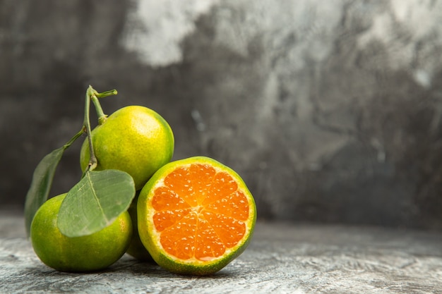 Horizontal view of fresh two whole green tangerines with leaves and one cut in half tangerine on gray background footage
