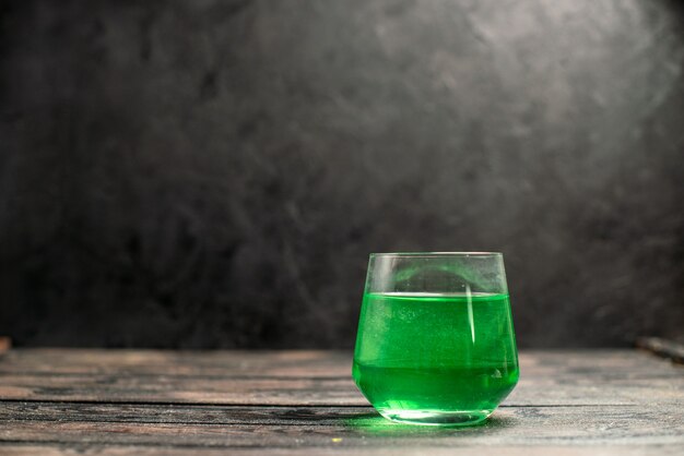 Horizontal view of green water in a glass lying on dark background