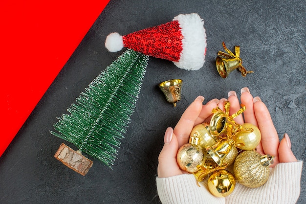 Foto gratuita vista orizzontale della mano che tiene la decorazione degli accessori albero di natale del cappello di babbo natale su uno sfondo scuro