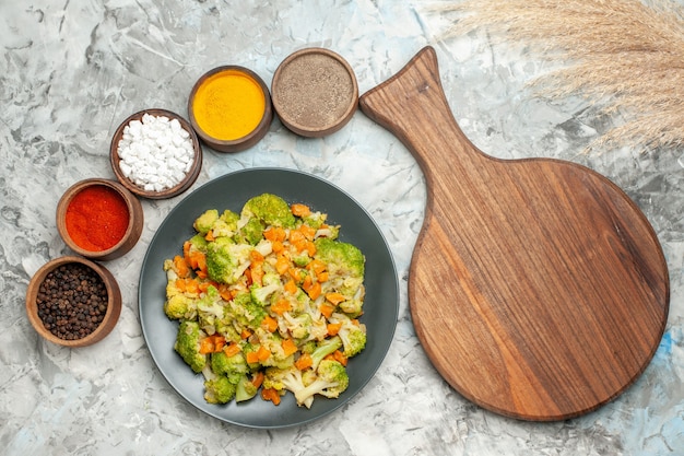 Horizontal view of healthy vegetable salad different spices and cutting board on white table