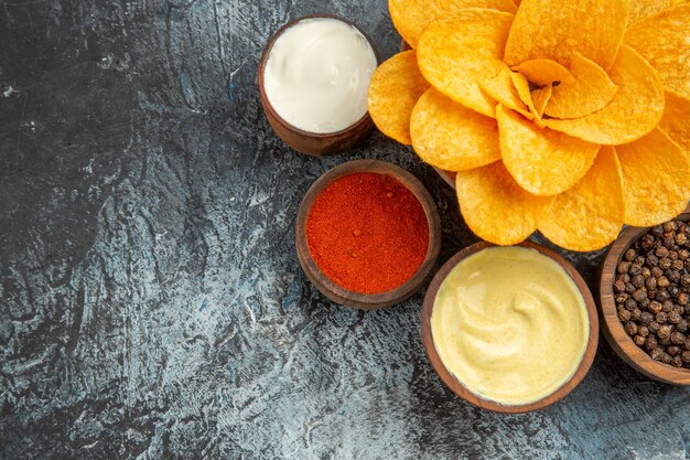 Horizontal view of homemade potato chips decorated like flower shaped and different spices mayonnaise on gray table
