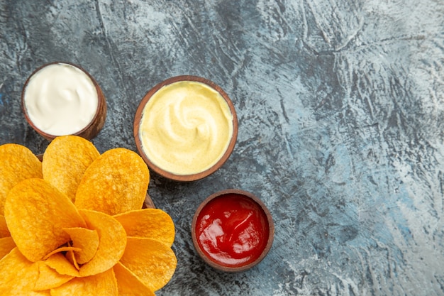 Horizontal view of homemade potato chips decorated like flower shaped and salt with ketchup mayonnaise on gray table
