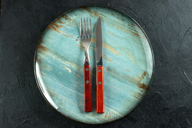 Horizontal view of meal cutlery on a blue plate on dark surface