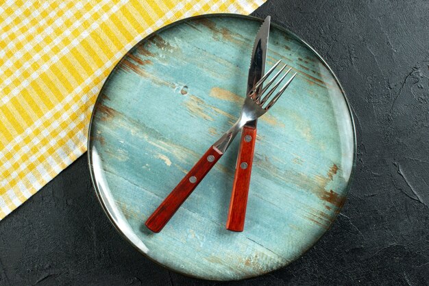 Horizontal view of meal cutlery in cross on a blue plate and yellow stripped towel on dark surface