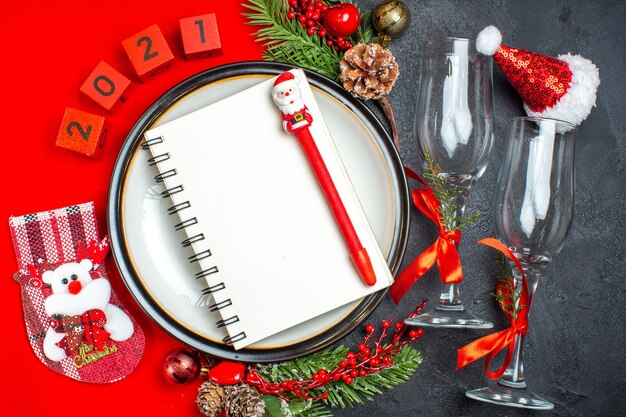 Horizontal view of notebook on dinner plates decoration accessories fir branches xsmas sock glass goblets on dark table