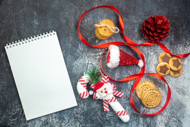 Horizontal view of notebook and santa claus hat and cornel chocolate red conifer cone gift cookies on dark surface