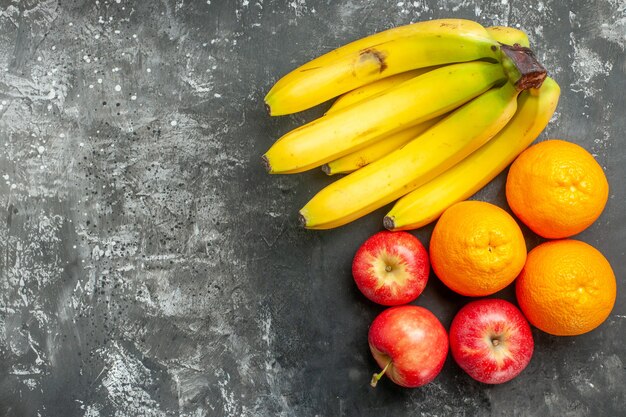 Horizontal view of organic nutrition source fresh bananas bundle and red apples an orange on the left side on dark background