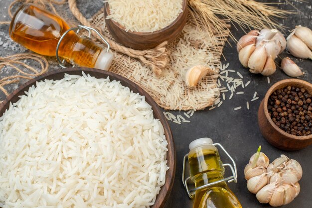 Horizontal view of perfect long rice brown bowls on nude color towel fallen oil bottles garlics peppers on dark background