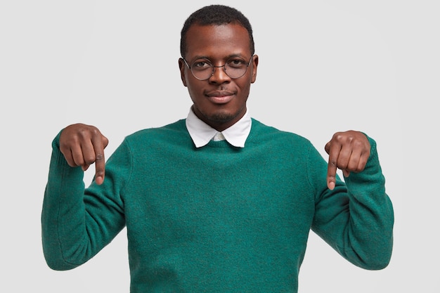 Free photo horizontal view of pleased dark skinned guy demonstrarates something down on floor, points with both index fingers