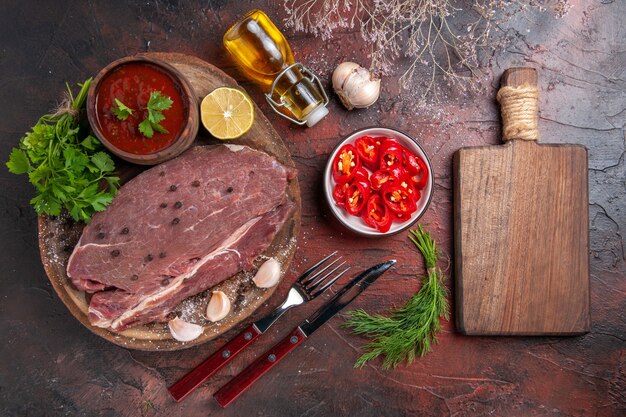 나무 쟁반에 있는 붉은 고기와 마늘 그린 케첩, 잘게 썬 후추 오일 병, 어두운 배경에 커팅 보드의 수평 보기