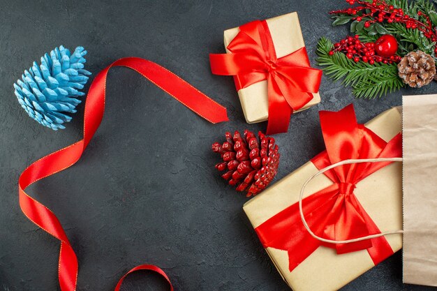 Horizontal view of a roll of red ribbon conifer cones and gift fir branches on dark table